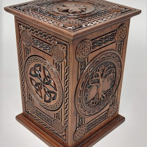 May include: A wooden box with intricate carvings of Celtic knots and a tree of life design. The box is a rich brown color and has a square shape.