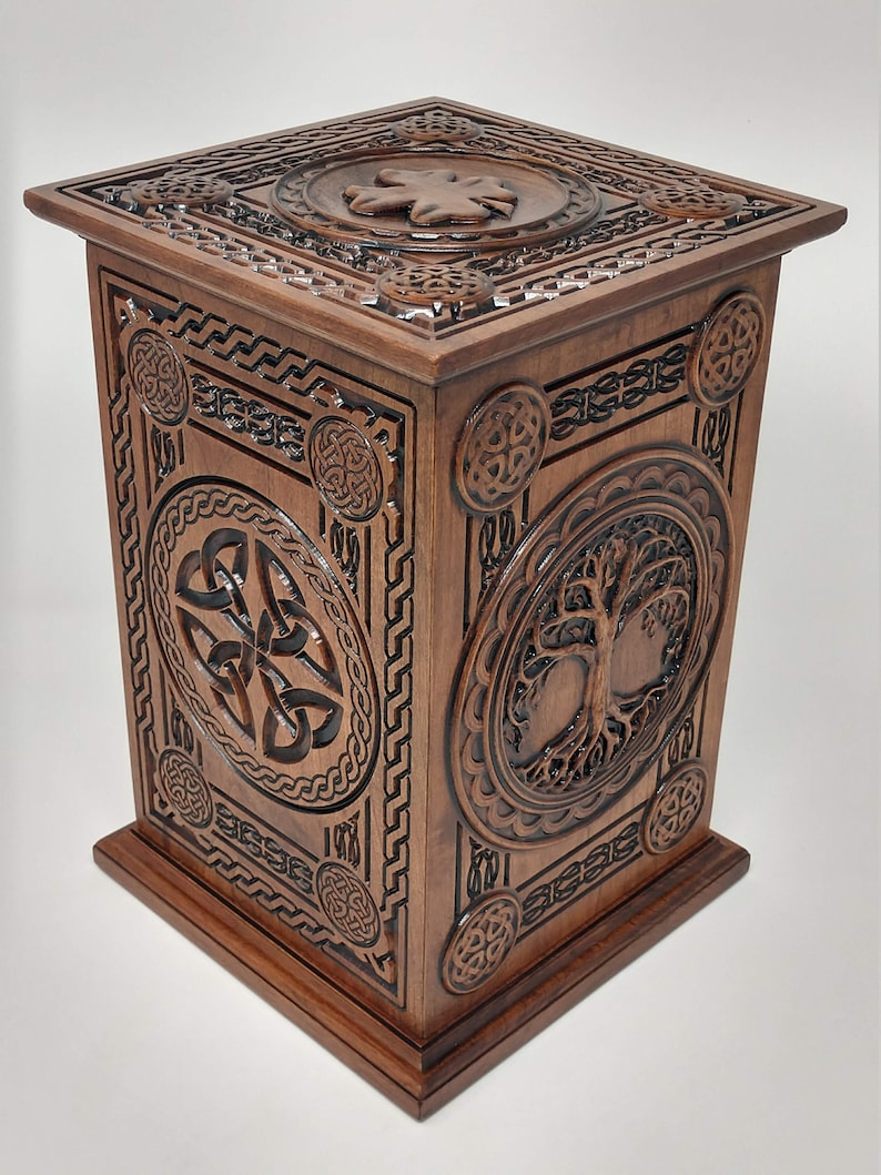 May include: A wooden box with intricate carvings of Celtic knots and a tree of life design. The box is a rich brown color and has a square shape.