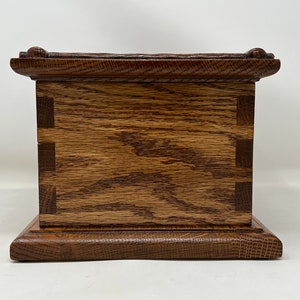 May include: A wooden box with a dark brown stain. The box has a raised base and a decorative top edge. The box is made of solid wood with visible grain.