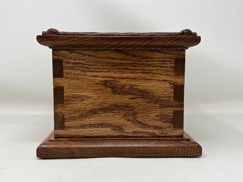May include: A wooden box with a dark brown stain. The box has a raised base and a decorative top edge. The box is made of solid wood with visible grain.