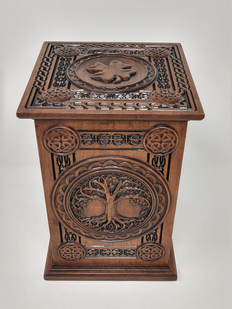 May include: A wooden box with intricate carvings of Celtic knots and a tree of life design. The top of the box features a carved shamrock.