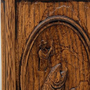 May include: A wooden plaque with a carved image of a fisherman holding a fishing rod and a large fish. The plaque is dark brown with a natural wood grain.