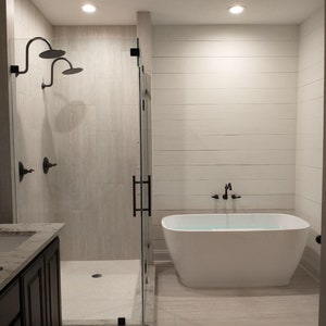 May include: A white bathtub with a black faucet and a shower with a white tiled floor and a white tiled wall.