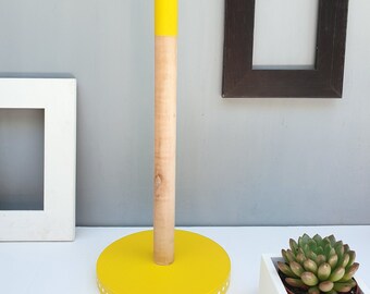 May include: Yellow paper towel holder with a white polka dot base and a wooden dowel. The holder is on a white surface.