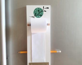 Pode incluir: Suporte de bloco de notas de madeira branco com um design de folha verde e um rolo de papel branco. Um lápis amarelo está preso ao suporte.