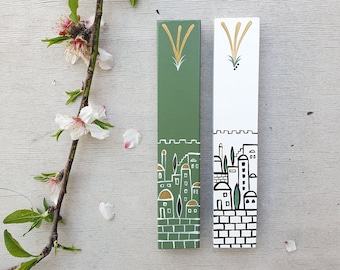 Pode incluir: Duas mezuzá de madeira com fundo verde e branco. As mezuzá apresentam um horizonte da cidade estilizado com detalhes dourados e um design de planta verde.
