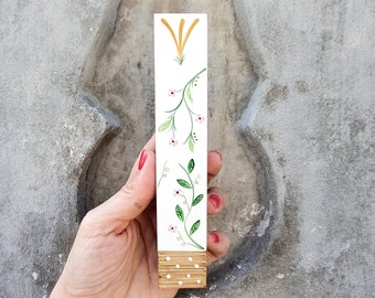 Pode incluir: Um marcador de página de madeira branco com um design floral pintado à mão. O design apresenta folhas verdes, flores cor-de-rosa e um caule amarelo.