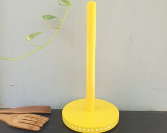 May include: A yellow wooden paper towel holder with a white polka dot trim. The holder is standing on a black surface.