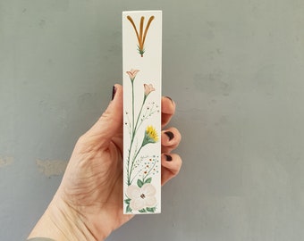 Pode incluir: Um bloco de madeira branco com um desenho floral pintado à mão. O desenho apresenta flores rosa, amarelas e verdes com caules marrons.
