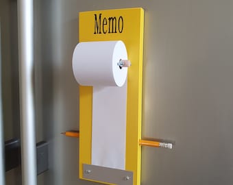 Pode incluir: Um quadro de memorandos amarelo com um rolo de papel branco e um lápis. A palavra "Memo" é impressa em preto no topo. Um segundo lápis é inserido horizontalmente através do quadro. Uma placa de metal está na parte inferior.