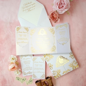 May include: Elegant wedding invitation suite with gold foil details on white cardstock. Includes invitation, RSVP cards, and envelope with script text. Features floral accents and vintage binoculars on a pink background.