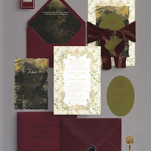 May include: A collection of wedding stationery in burgundy, gold, and olive green. Includes invitations, envelopes, and a ring box. The invitation features the names "Gabrielle Noel" and "Gilbert Soriano". A glass of champagne with a gold rose stirrer is also present.