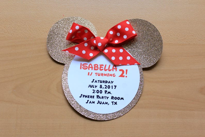May include: A Mickey Mouse-themed birthday invitation. The invitation is shaped like Mickey's head, with gold glitter ears and a red bow with white polka dots. The invitation reads "Isabella is turning 2!" with party details.