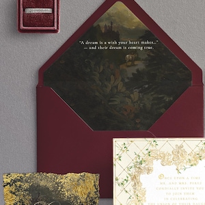 May include: A wedding invitation suite featuring a burgundy envelope with a landscape painting inside, a ring in a burgundy box, and a details card with gold accents. The invitation includes the text: "Once upon a time..." and "A dream is a wish your heart makes..."