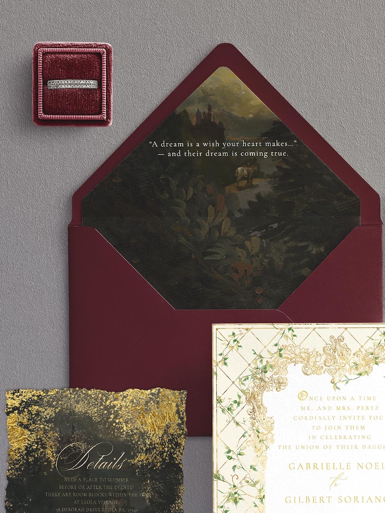 May include: A wedding invitation suite featuring a burgundy envelope with a landscape painting inside, a ring in a burgundy box, and a details card with gold accents. The invitation includes the text: "Once upon a time..." and "A dream is a wish your heart makes..."