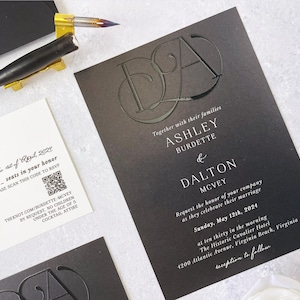 Op de afbeelding: Elegante zwarte trouwuitnodiging met reliëf initialen en evenementdetails. Inclusief een bijpassende RSVP-kaart en een pen voor kalligrafie. De uitnodiging toont de namen Ashley Burdette en Dalton McVey, met de trouwdatum en -locatie.