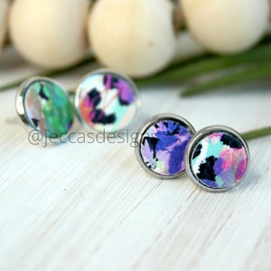 May include: A set of three pairs of colourful floral fabric stud earrings. The earrings are silver-toned and have a round shape. The fabric is a mix of pink, purple, blue, and green.