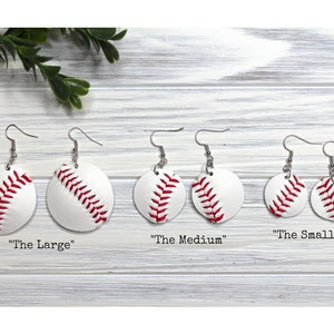 May include: Set of three pairs of white and red baseball earrings. The earrings are in three sizes: "The Large", "The Medium", and "The Small".