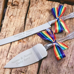 May include: A set of two silver cake knives with clear handles and rainbow ribbon bows. The knives are engraved with "Name & Name Date here".