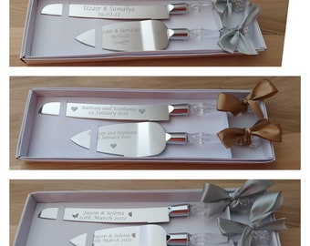 May include: Two sets of silver cake knives with engraved names and dates in a white box with a silver ribbon. The knives are in a clear plastic case with a silver bow.