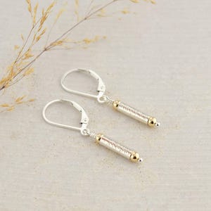 May include: A pair of silver earrings with gold accents. Each earring features a textured, cylindrical pendant with a small gold bead at the end.