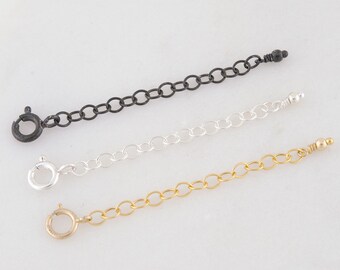 May include: Three necklace extender chains in black, silver, and gold. Each chain has a spring ring clasp on one end and a small bead or decorative end on the other. The chains are displayed on a white surface.