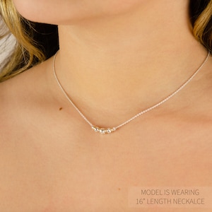 Puede incluir: Un delicado collar de cadena plateada con un peque&ntilde;o grupo de cinco cuentas met&aacute;licas en el centro. El collar tiene una longitud total de 16 pulgadas, como indica el texto en la imagen. Las cuentas alternan entre tonos plateados y dorados.