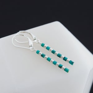 May include: A pair of silver dangle earrings with turquoise beads. The earrings are long and slender, with a simple design.