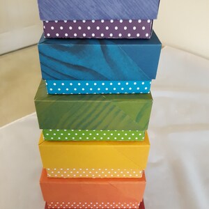 May include: A stack of six colorful boxes with white polka dot trim. The boxes are arranged in a rainbow pattern, starting with purple and ending with red.