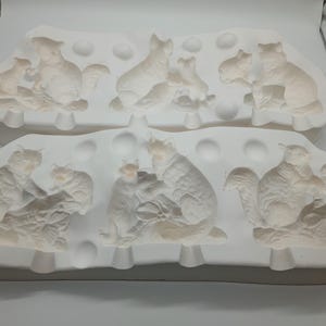 May include: A white ceramic mould with multiple cavities for making squirrel figurines. The mould is divided into two sections, each with a different design. The mould is made of a smooth, white ceramic and has a slightly textured surface.