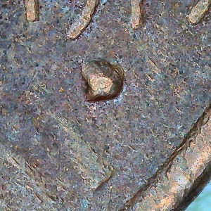 May include: Close-up of a copper penny with a small, raised bump on the surface. The penny is worn and has a greenish patina.