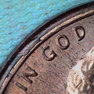May include: Close-up of a copper penny with the inscription "IN GOD WE" visible. The coin is slightly worn and has a patina.