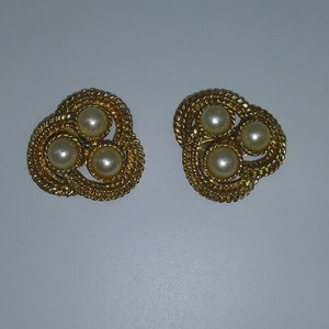 May include: A pair of gold tone clip-on earrings with three faux pearl accents each.