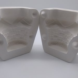 Op de afbeelding: Twee witte keramische mallen voor het gieten van een gedetailleerd ontwerp. De mallen zijn open en laten het ingewikkelde ontwerp zien.