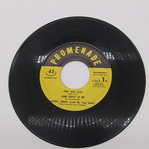 Peut inclure: Un disque vinyle noir de 45 tours avec une étiquette jaune. L'étiquette comporte le texte "PRO-ME-N-A-D" dans un cercle jaune avec une bordure noire. Le texte "EXTENDED PLAY" est en texte noir sous le cercle. Le texte "NON-BREAKABLE (with normal use)" est en texte noir sur le côté droit de l'étiquette. Le texte "A-54-8 1A" est en texte noir sous le texte "NON-BREAKABLE". Le texte "With the PROMENADE Orch. & Chorus" est en texte noir sous le texte "A-54-8 1A". Le texte "PINK SHOE LACES Janet King COME SOFTLY TO ME The Grasshoppers KOOKIE, KOOKIE (Lend Me Your Comb) Richard Deane & Jennie Feathers" est en texte noir au bas de l'étiquette.
