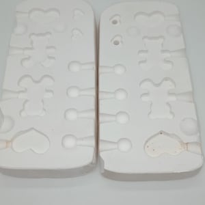 May include: Two white silicone molds for making small resin crafts. The molds are divided into sections with different shapes, including hearts, bears, and small round shapes.