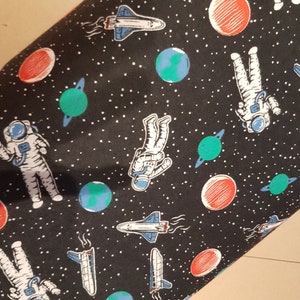 Könnte beinhalten: Schwarzer Stoff mit Weltraum-Motiv. Das Design umfasst Astronauten, rote und grüne Planeten, blau-weiße Raumfähren und weiße Sterne. Geeignet für Näh- oder Bastelprojekte.