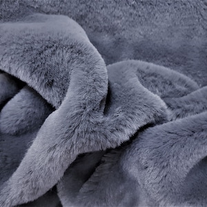 May include: Close-up of a soft, plush, gray faux fur fabric. The fabric has a short pile and a slightly textured surface.