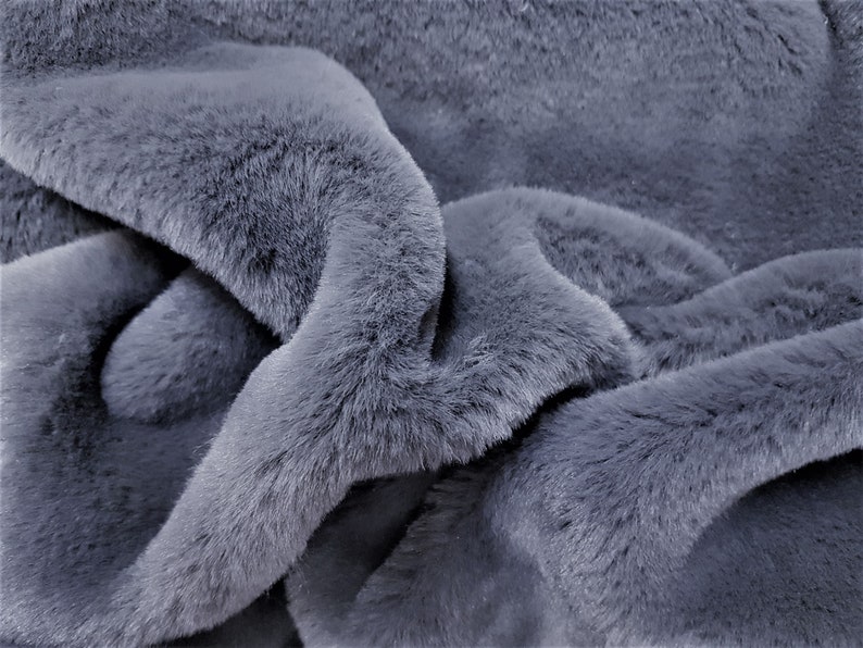 May include: Close-up of a soft, plush, gray faux fur fabric. The fabric has a short pile and a slightly textured surface.
