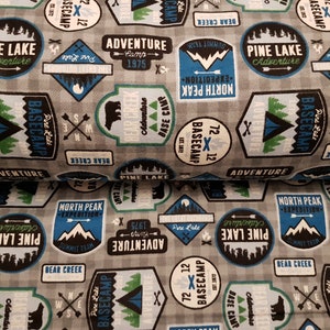 Könnte beinhalten: Ein grauer und weißer karierter Stoff mit einem sich wiederholenden Muster aus blauen und grünen Camping-Motiven. Die Patches zeigen Texte wie "Pine Lake Adventure", "Basecamp", "North Peak Expedition" und "Adventure Camp 1975".