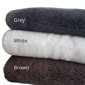 May include: Three faux fur fabric swatches in grey, white, and brown. The swatches are stacked on top of each other.