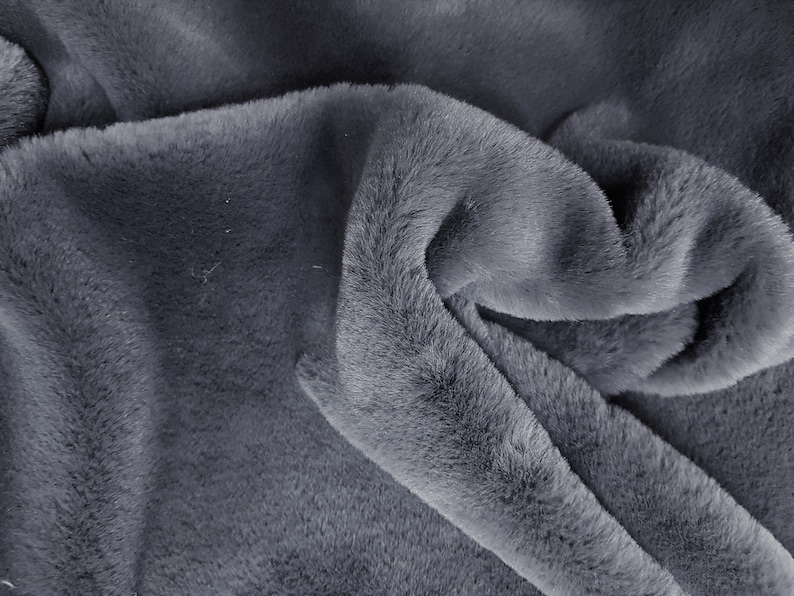 May include: Close-up of a soft, gray faux fur fabric. The fabric is folded and draped, showing the texture and pile of the material.