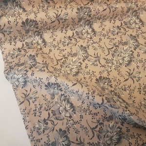 Puede incluir: Una tela beige con un patrón floral en tonos grises. Las flores son un diseño estilizado con un aspecto ligeramente descolorido.