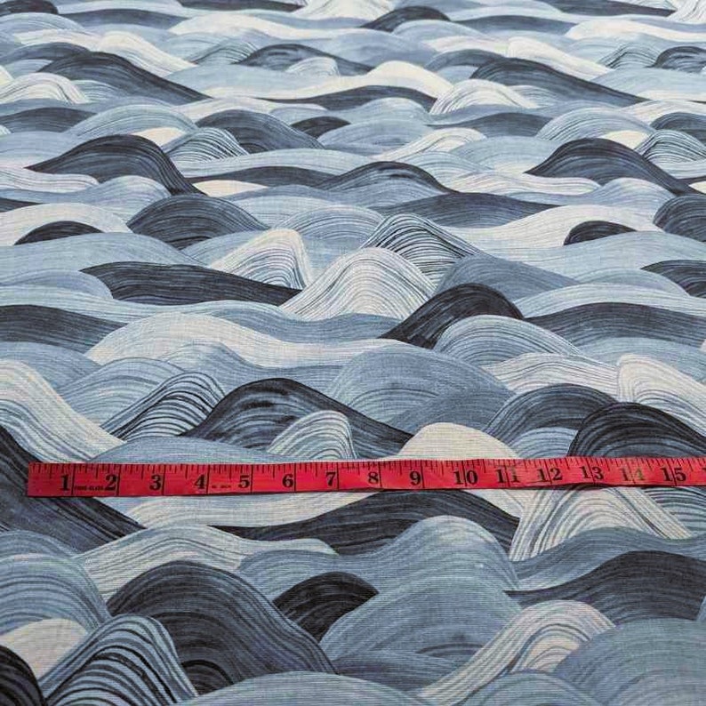 May include: Fabric with a repeating wave pattern in shades of blue, white, and gray. A red measuring tape is placed across the bottom, showing measurements up to 15 inches.