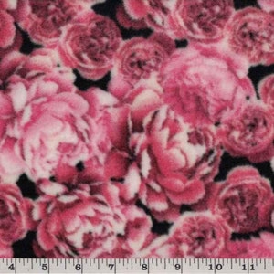 Könnte beinhalten: Rosa-weißer Blumenstoff mit schwarzem Hintergrund. Der Stoff hat eine flauschige Textur und zeigt ein sich wiederholendes Muster aus großen, stilisierten Rosen.