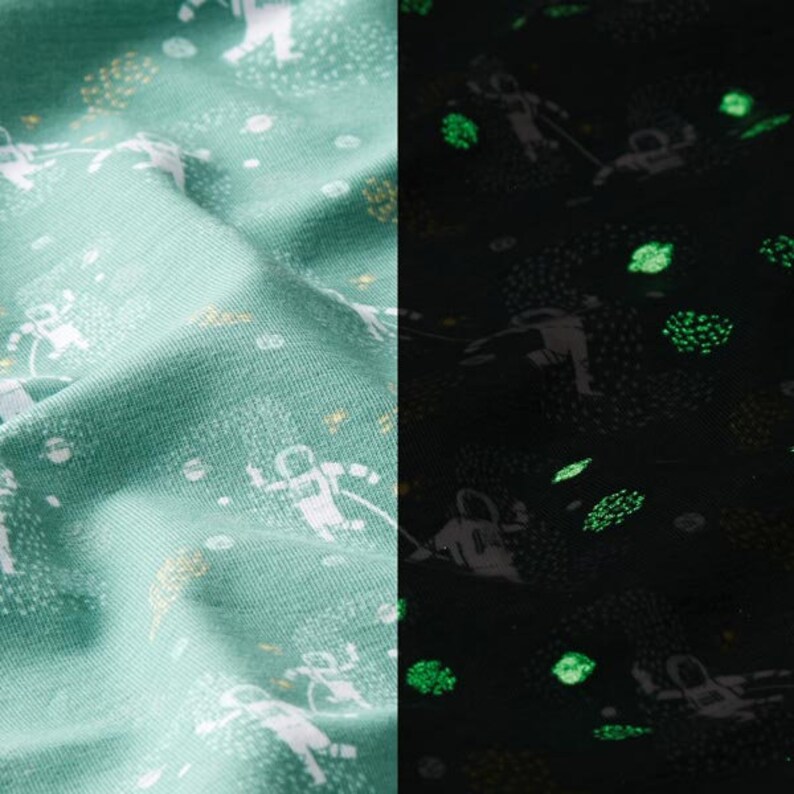 Puede incluir: Una tela verde con un estampado blanco de astronautas y estrellas. La tela brilla en la oscuridad, revelando un estampado verde de astronautas y estrellas.