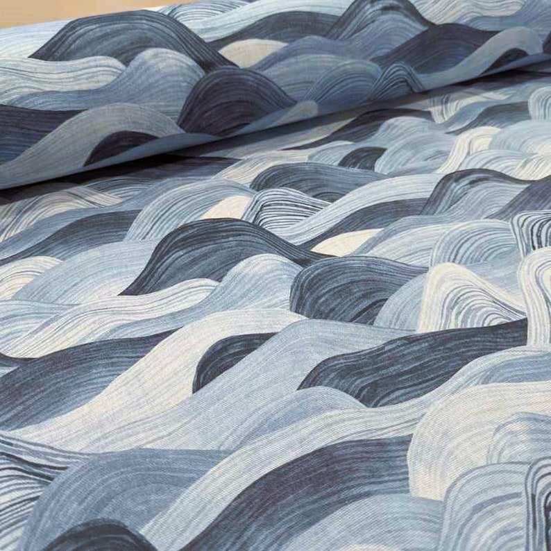May include: Close-up of fabric with a wave-like pattern in shades of blue and white. The design features flowing lines that create a textured, three-dimensional effect. The fabric appears to be folded, adding depth to the image.
