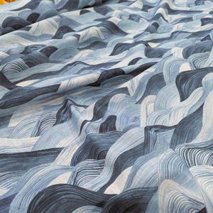 May include: Close-up of a fabric with a wave-like pattern in shades of blue and white. The design features flowing, curved lines that create a sense of depth and movement. The fabric appears to be soft and textured, suitable for various textile projects.