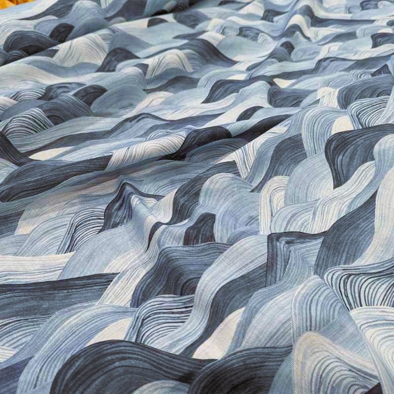 May include: Close-up of a fabric with a wave-like pattern in shades of blue and white. The design features flowing, curved lines that create a sense of depth and movement. The fabric appears to be soft and textured, suitable for various textile projects.