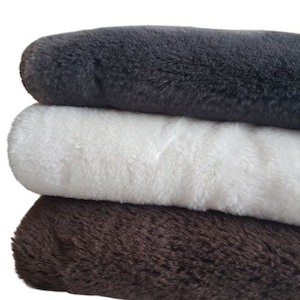 May include: Three faux fur fabric swatches in different colors: dark gray, white, and brown. The swatches are stacked on top of each other.